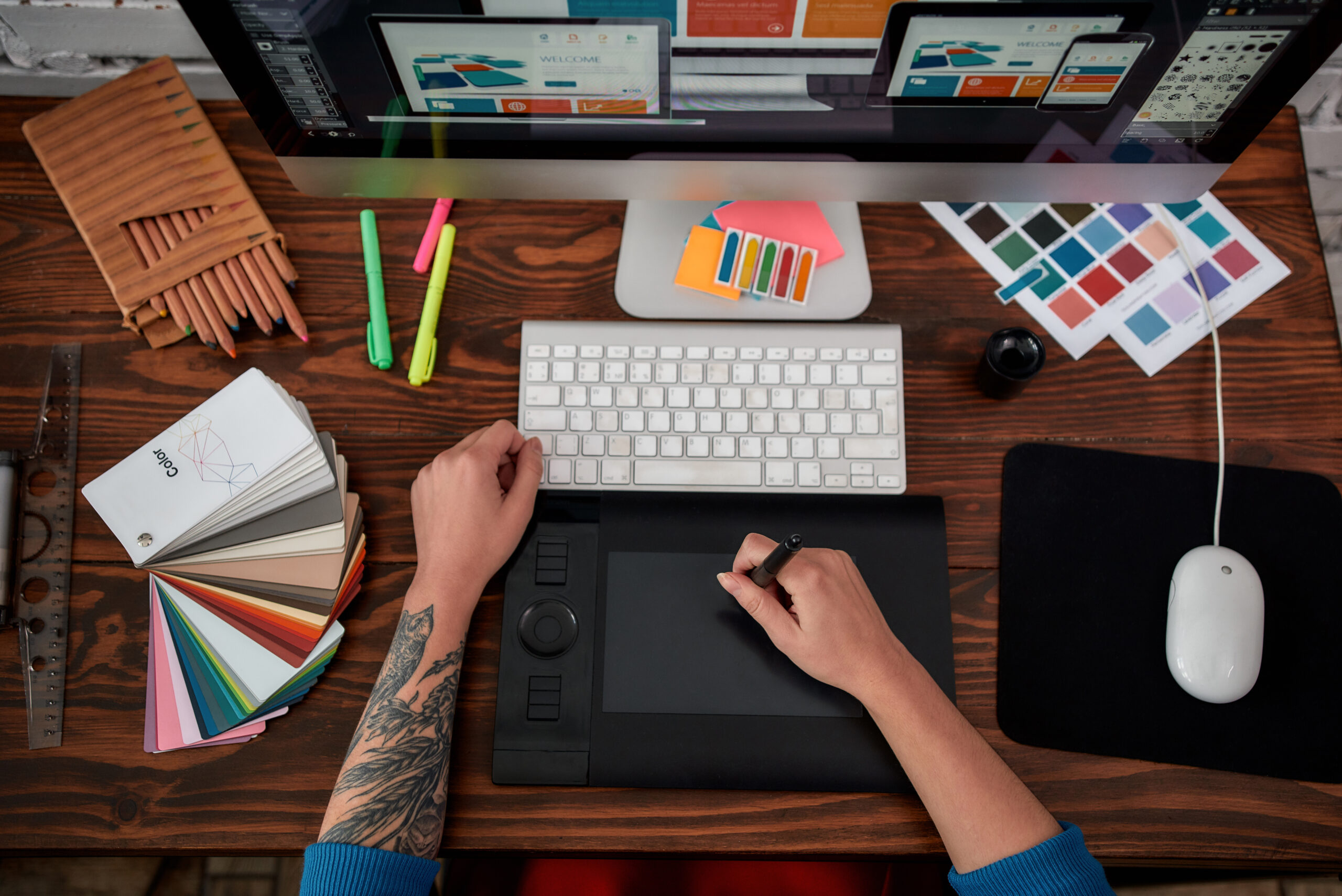 Top view of a graphic designer using graphic tablet and computer in the office or studio. Workplace with graphic tablet, keyboard, computer and color swatches. Creative occupation